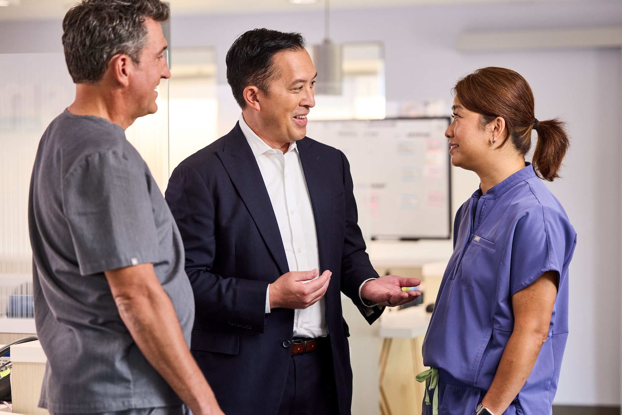 Three dentists in an office lobby, gesturing to each other in conversation.