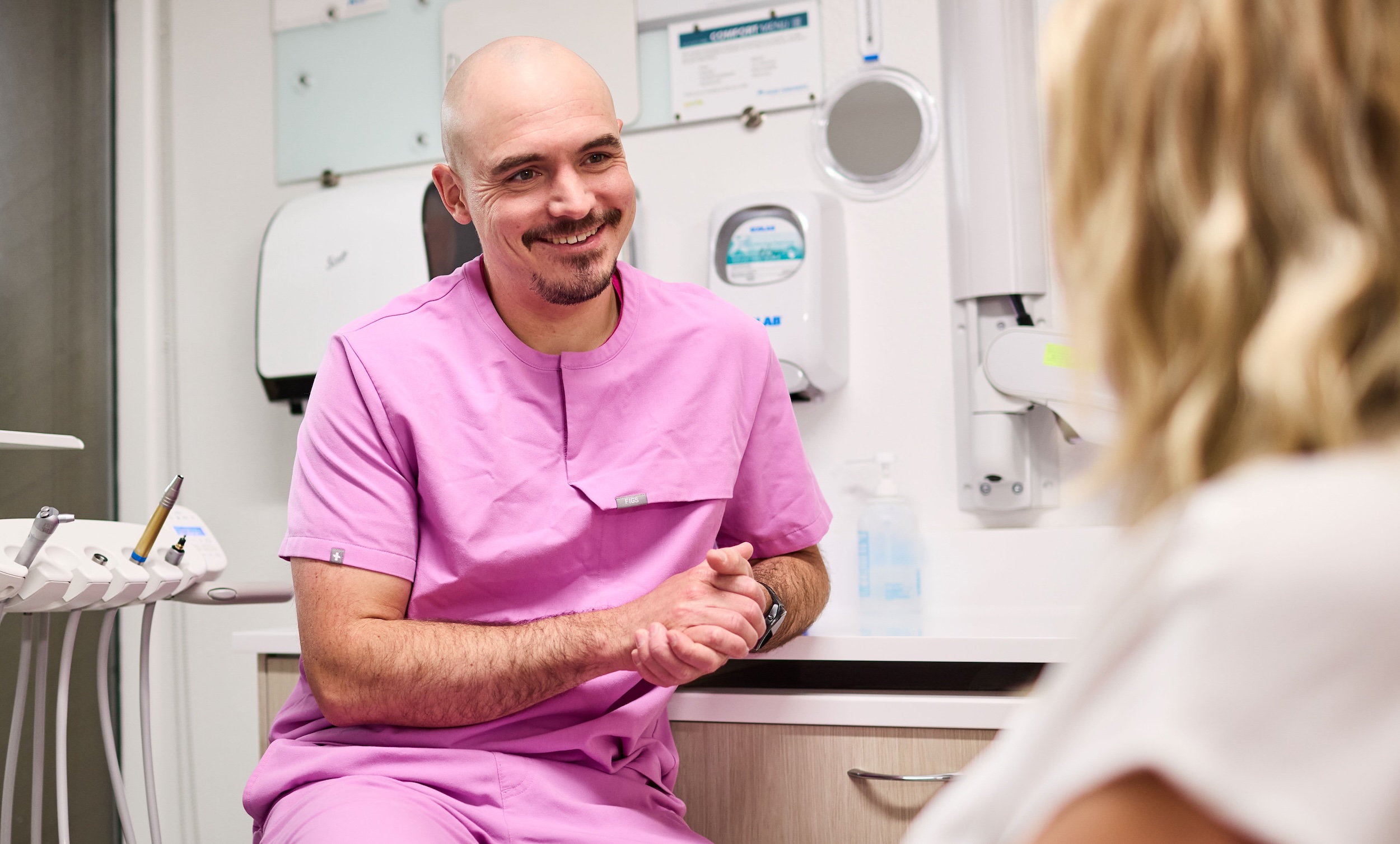 A dentist in pink scrubs smiling at a patient