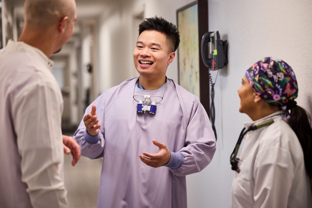 Three dentists wearing lab coats and gesturing in conversation
