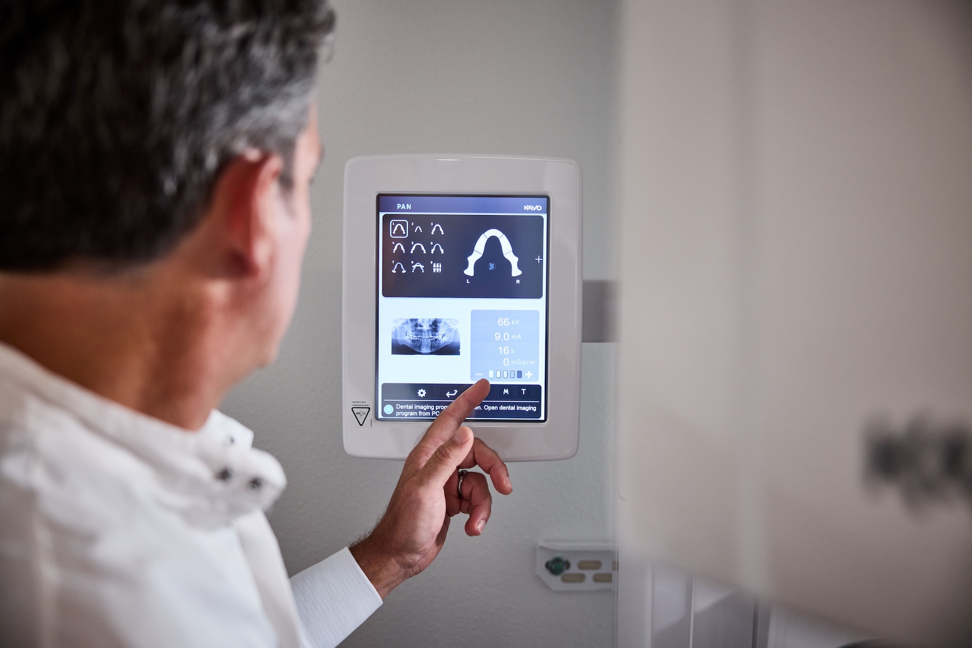 A close up of a dentist pointing at stats on an x-ray imaging screen